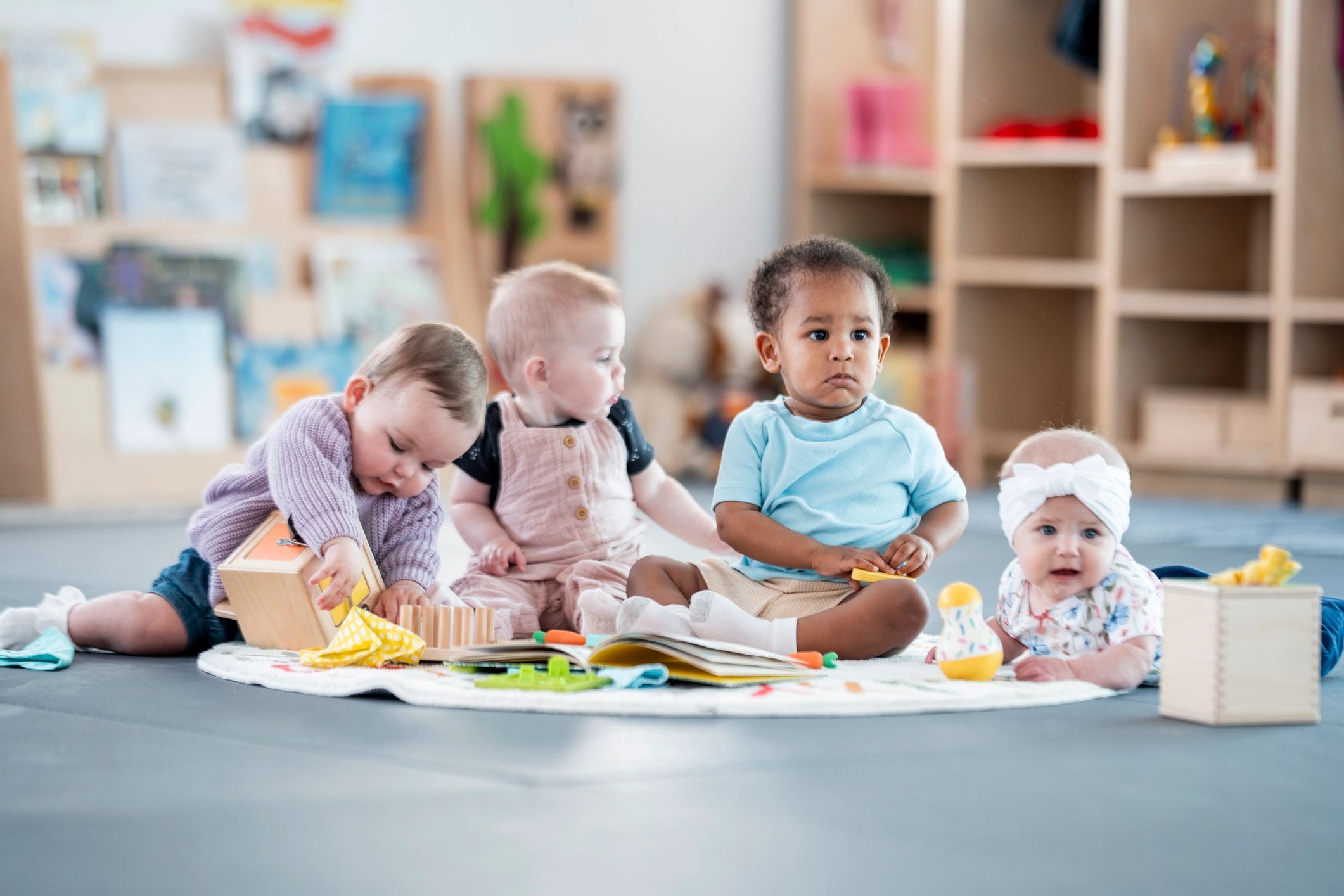 Four babies playing together on a mat.