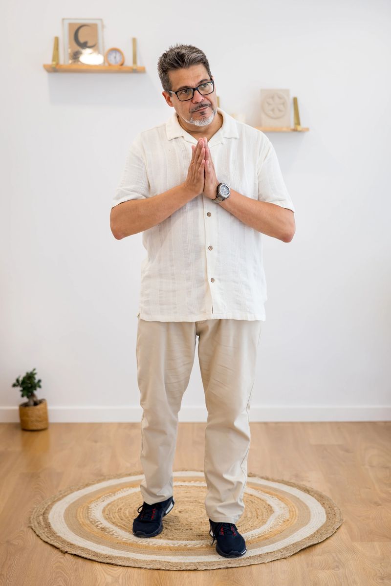 Mature therapist standing on a round rug with his hands together in a praying position, practicing alternative therapy in his bright office