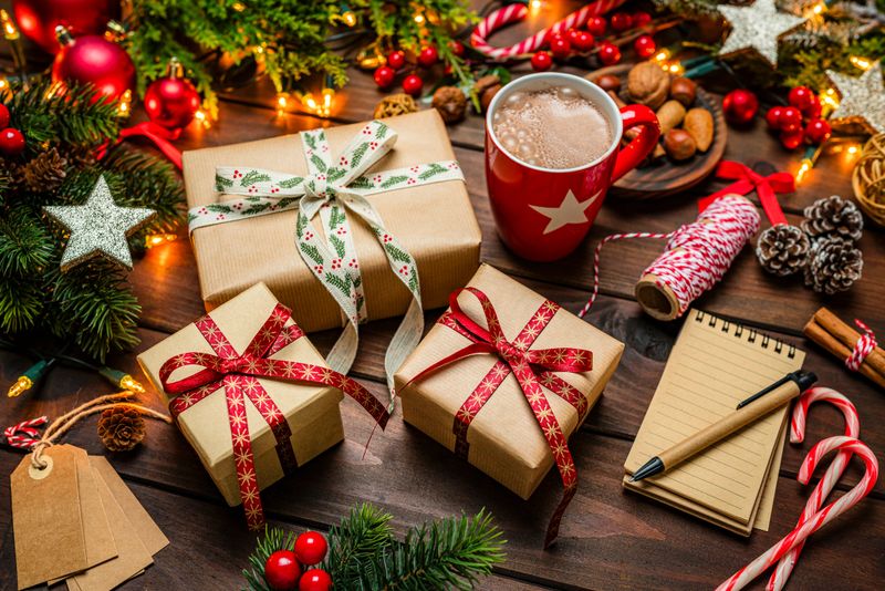 Christmas gift boxes background on wood table, wrapping or preparation. Ornaments, hot chocolate and candy canes. Cozy atmosphere, note pad and gift tags