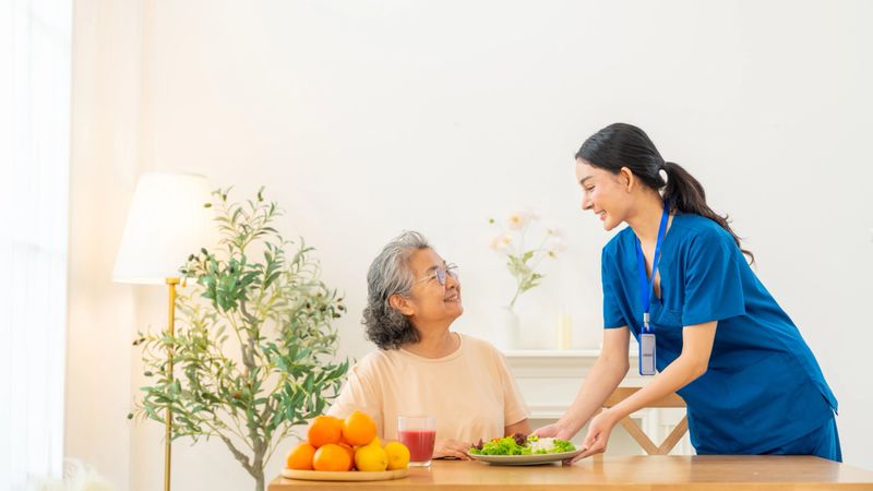 Female caregiver take care and serving healthy food organic salad to senior woman at nursing home. Retirement rehabilitation. Elderly people health, home medical wellness healthcare services concept.