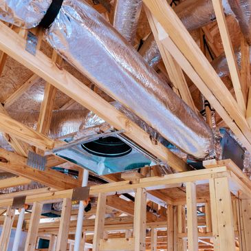 Insulated HVAC ducts installed in wooden framing of a building under construction.