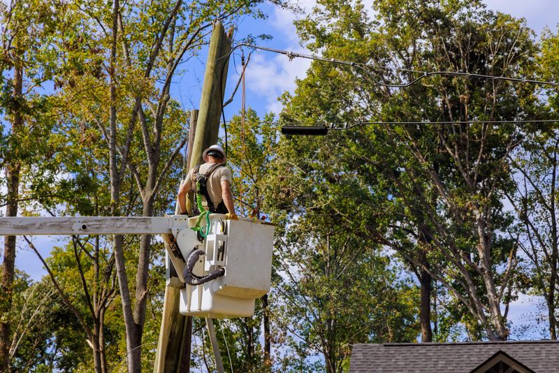 Utility worker stands in bucket lift fixing electrical lines above neighborhood with after hurricane