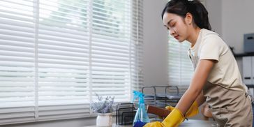 Woman cleaning a wooden desk with gloves and a spray bottle.