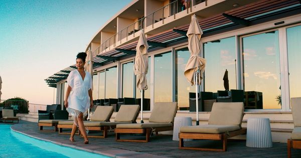 Woman in white walking barefoot by a poolside at sunset.