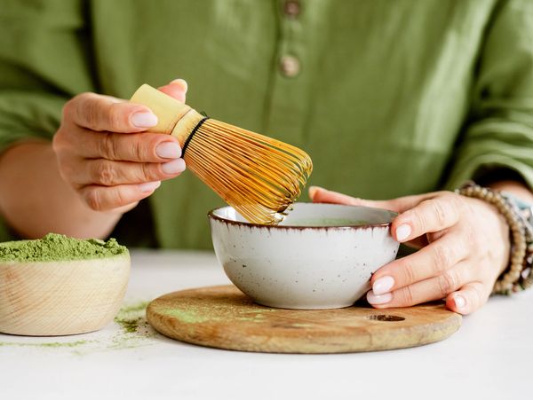 Person preparing matcha tea using a bamboo whisk and bowl.