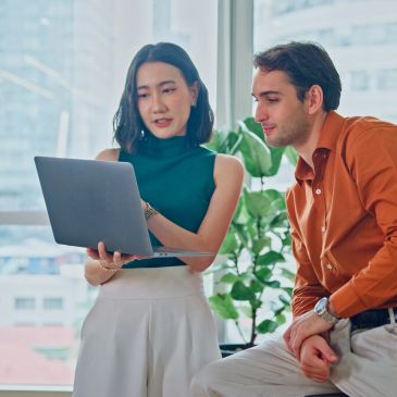 Two colleagues discussing work on a laptop in the office.