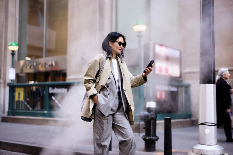 Young adult businesswoman using a smartphone while walking on a bustling New York City street, close to a subway entrance
