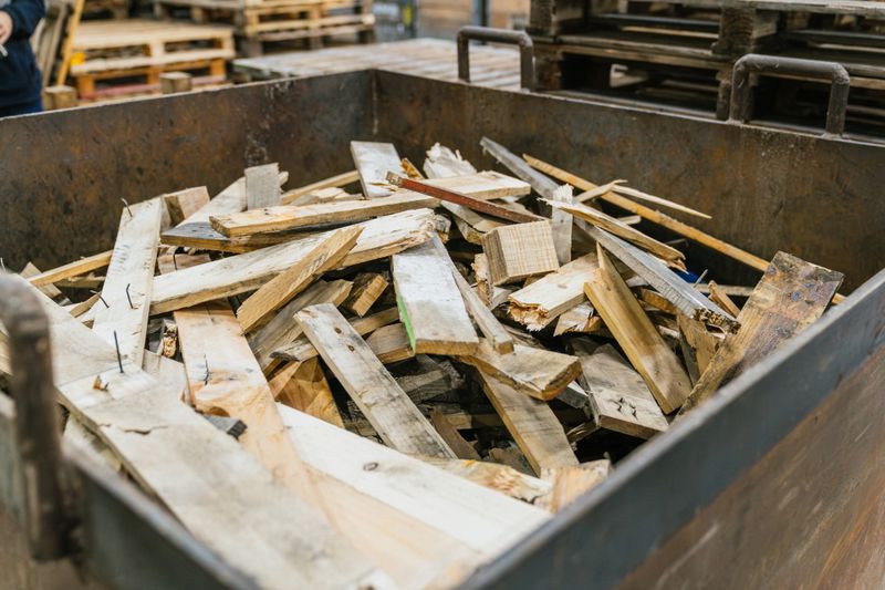Collecting scraps of wooden pallets in a large metal container, promoting recycling efforts within an industrial setting for sustainable practices