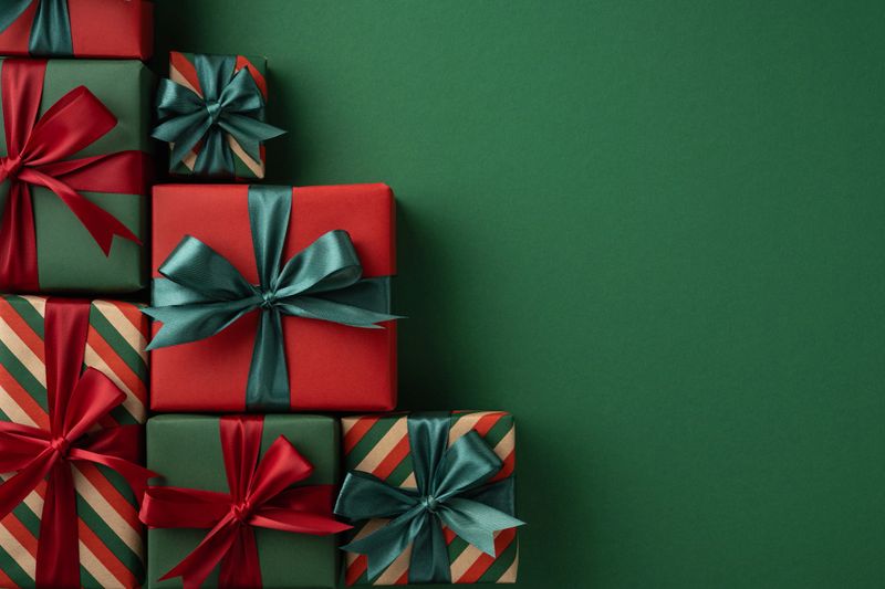 A collection of beautifully wrapped presents in red and green with vibrant ribbons, arranged against green festive background, symbolizing holiday joy, gifting traditions, and the Christmas  spirit