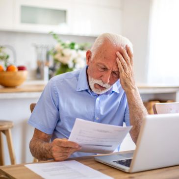 Elderly man stressed reading documents at home.