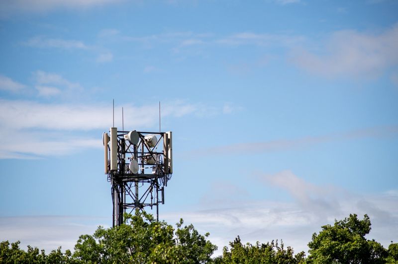 A mobile communication tower surrounded by green treetops under a bright blue sky. Modern technology and connectivity.