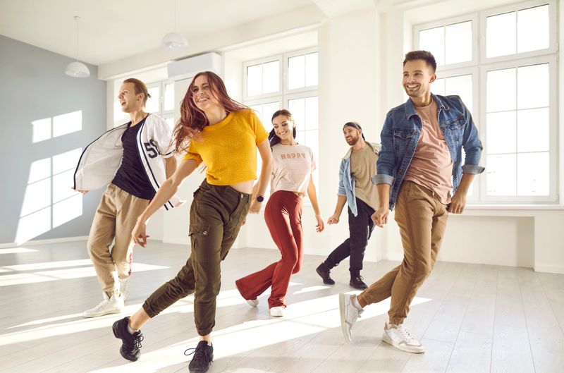 Group of happy beautiful young people enjoying a contemporary dancing class. Team of cheerful smiling dancers in casual wear practising a new choreo and having a good time together in a modern studio