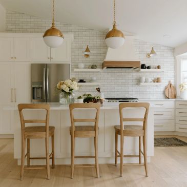 Bright modern kitchen with white cabinets, wooden chairs, and pendant lights.