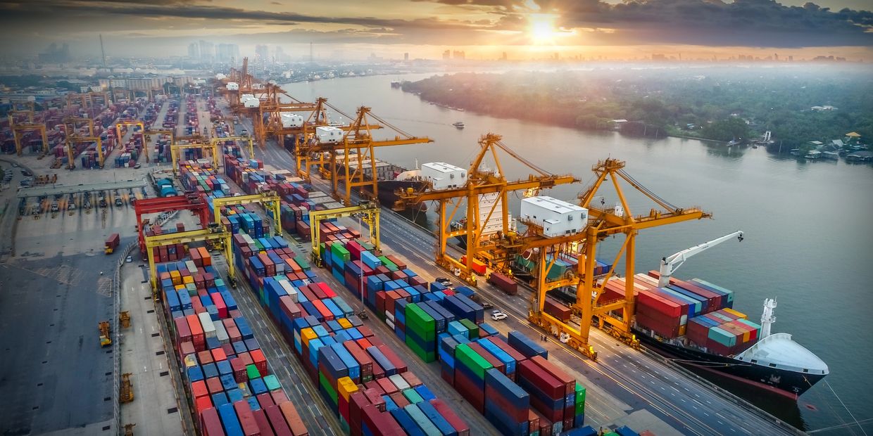 Sunset over a busy shipping port with containers and cranes.
