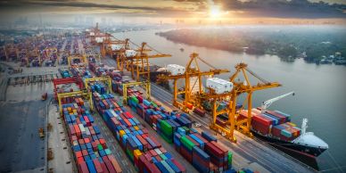 Shipping containers and cranes at a busy port during sunset.