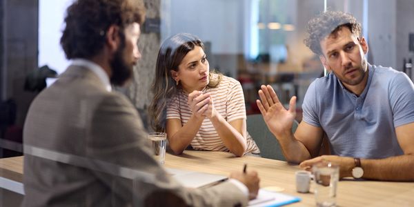 Three people engaged in a serious discussion around a table in an office.