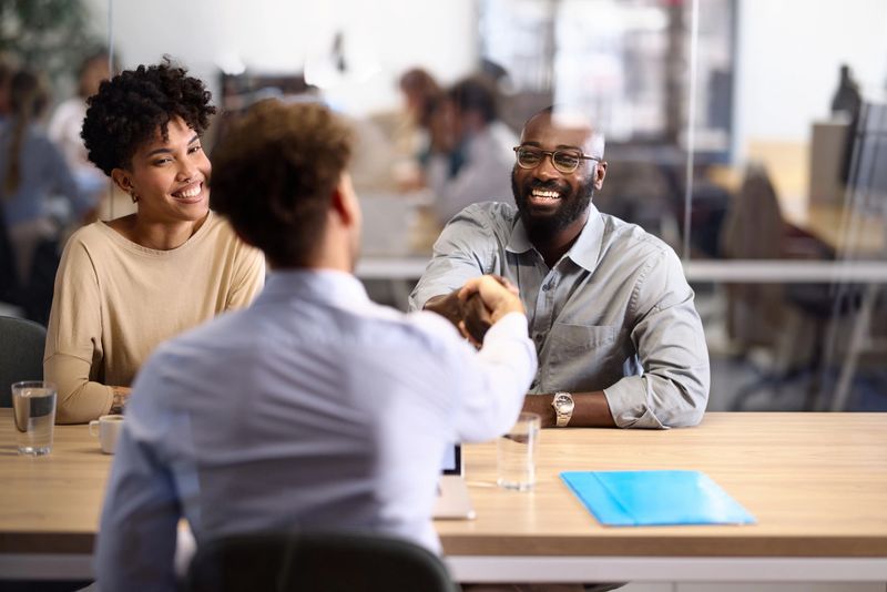 Happy African American couple came to a successful agreement with their insurance agent during a meeting in the office. The view is through glass.