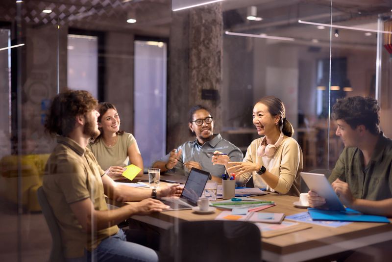 Group of happy creative colleagues communicating while working on a meeting at casual office. The view is through glass.