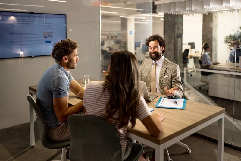 Happy mature insurance agent communicating with a couple during a meeting in the office. The view is through glass.