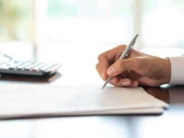 Person writing on a document with a pen at a desk.