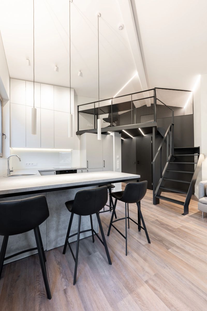 A sleek and contemporary loft apartment featuring an open kitchen layout with bar stools, a mezzanine workspace, and a clean minimalist design. Modern Luxury Home Loft Apartment Kitchen Interior