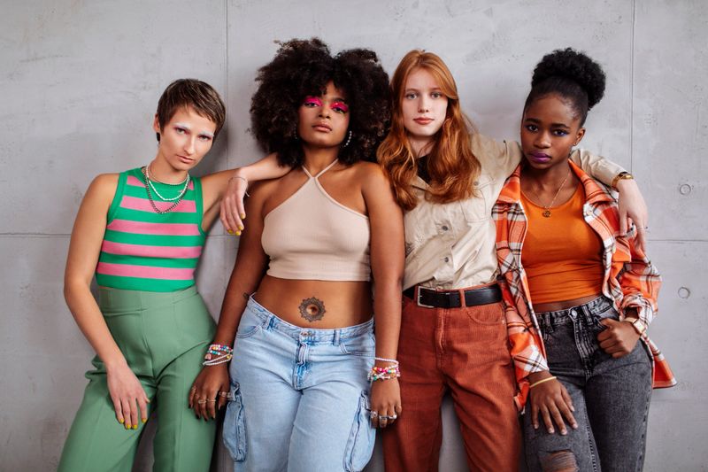 Four diverse Gen Z teenage girls with unique styles pose confidently in a photography studio, showcasing vibrant outfits, bold makeup, and modern fashion sensibilities