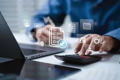 Person using calculator and laptop with digital icons floating.