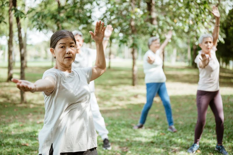 A diverse group of older adults performing tai chi exercises in a peaceful park setting. The seniors stand with focused expressions and graceful movements, promoting physical fitness, mindfulness, and healthy aging through gentle outdoor exercise.