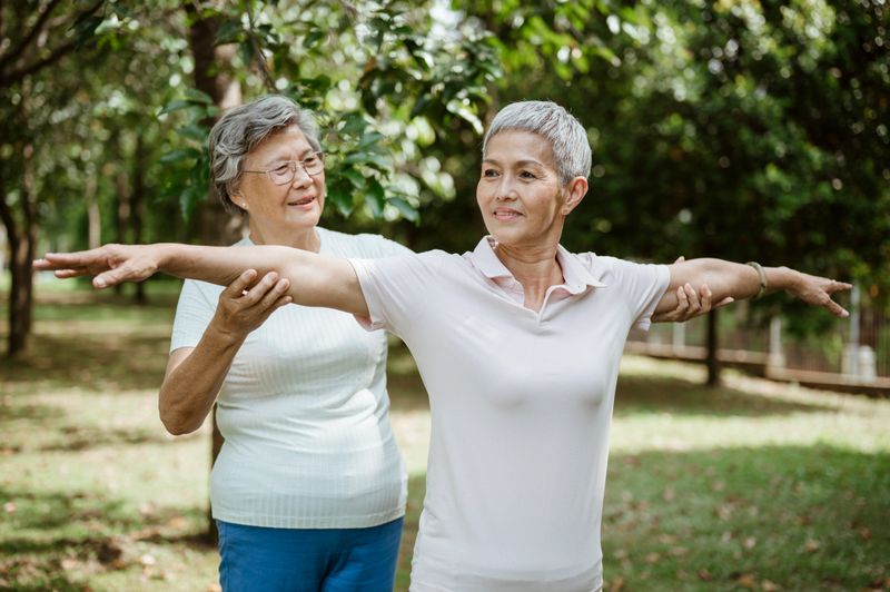 Under the shade of leafy trees, a group of senior Asian women engage in Tai Chi, focusing on fluid, meditative movements. Their practice highlights the timeless value of Tai Chi in enhancing balance, reducing stress, and cultivating inner peace.