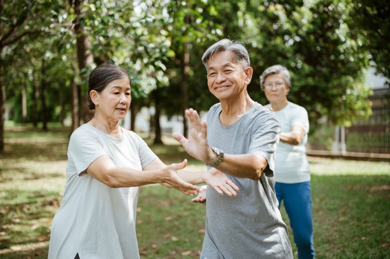 Elderly men and women performing tai chi in a calm, sunlit park. The early morning routine supports physical strength, flexibility, and emotional well-being, while reinforcing the importance of social connection in later years.
