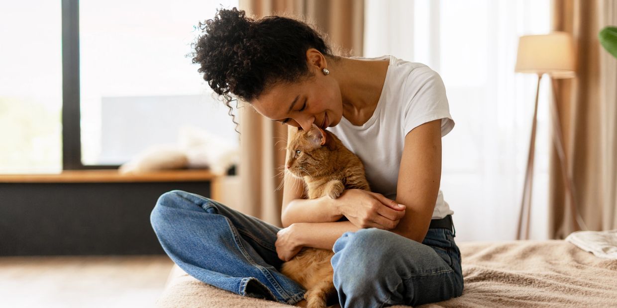 Woman in white shirt cuddling an orange cat on a bed.