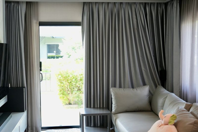 A modern, comfortable living room sliding glass door opening to a bright patio or garden.Gray L-shaped sofa with plush cushions in foreground, home interiors, real estate, modern living,home concept.