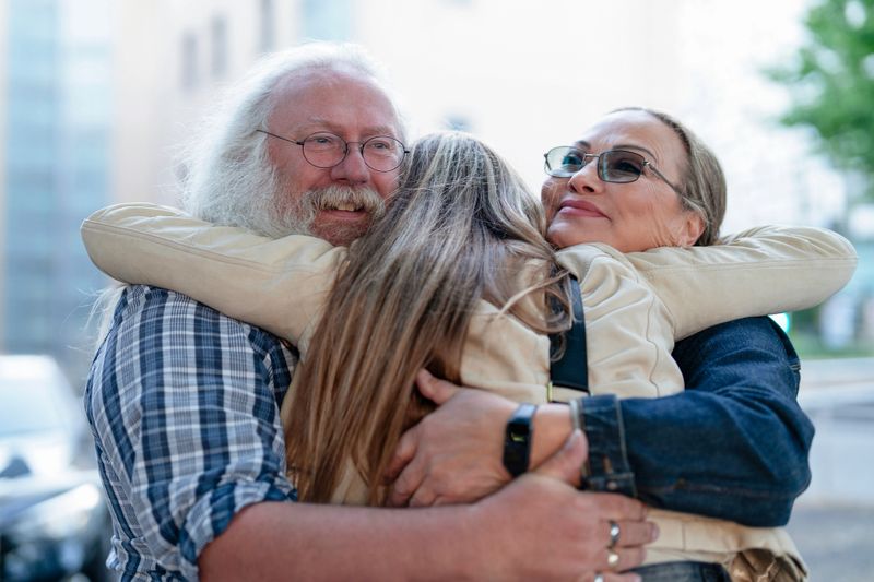 Two grandparents joyfully embrace their grandchildren in a city park, sharing a heartfelt moment under the warm sunlight on a beautiful afternoon.