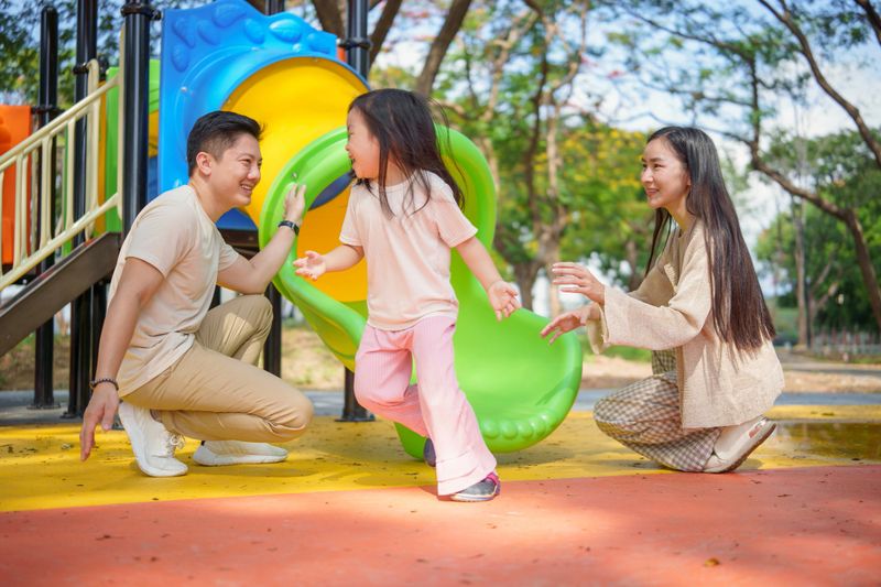 Happy family enjoying playtime with their daughter at a colorful playground.