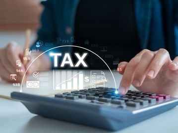 Person calculating taxes using a calculator with digital tax graphics.