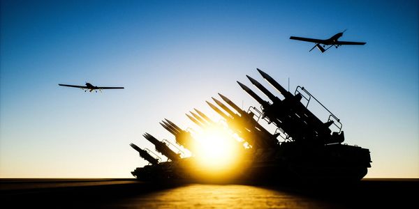 Military drones flying over missile launchers at sunset.