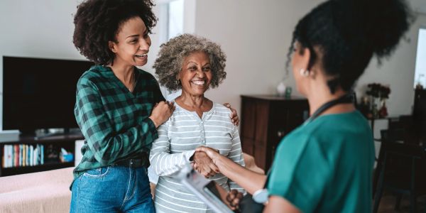 Smiling elderly woman with her daughter greeting a healthcare worker.