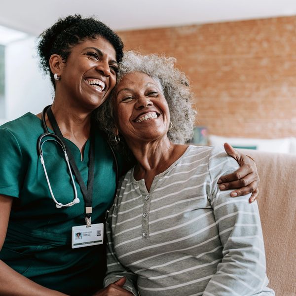 Nurse and elderly woman share a joyful embrace and smile indoors.