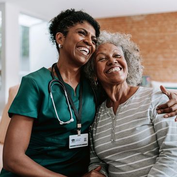 Nurse and elderly woman smiling and embracing warmly indoors.
