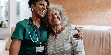 A nurse and elderly woman share a joyful hug indoors.