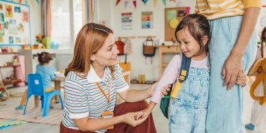 Teacher greeting a young girl at school.