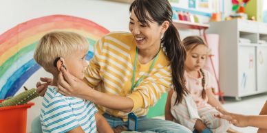 Teacher checks boy's ears in colorful classroom.