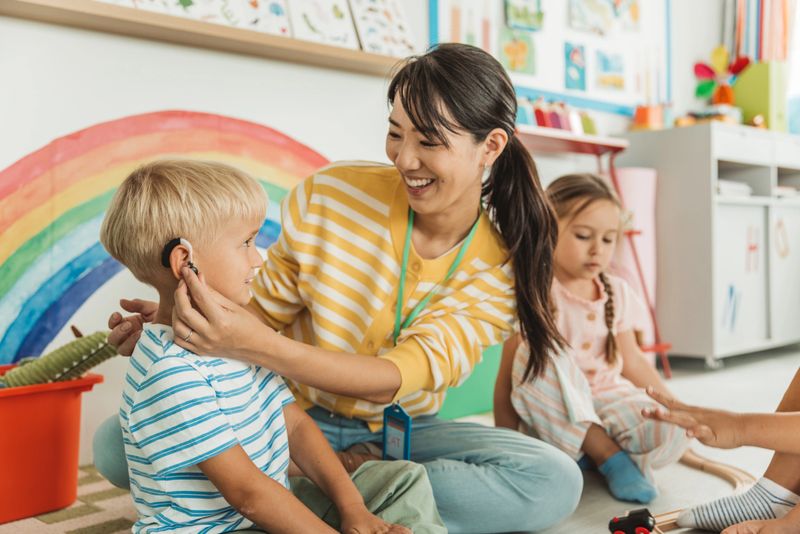 Schoolboy in kindergarten with a hearing aid playing with toys and friends.