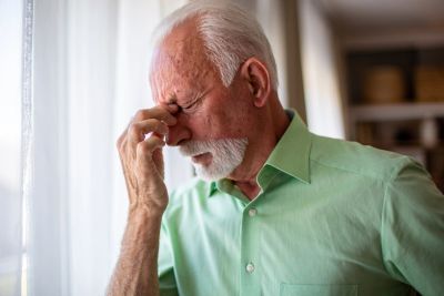 An older man suffering from vertigo with his eyes closed and a hand to the center of his head.