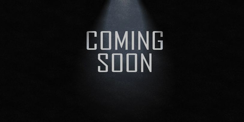 Coming soon text under spotlight on dark background.