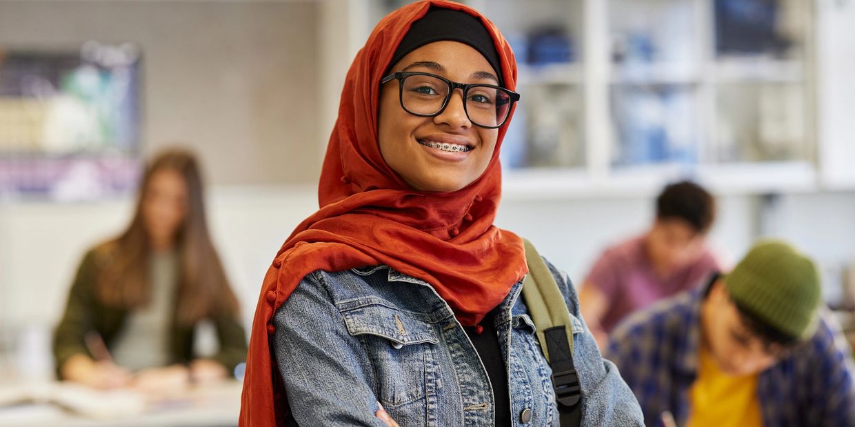 Femme souriante portant un hijab rouge et des lunettes en classe.
