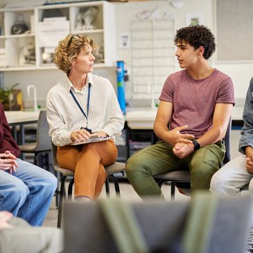 A group therapy session with a counselor and teenagers engaged in conversation.