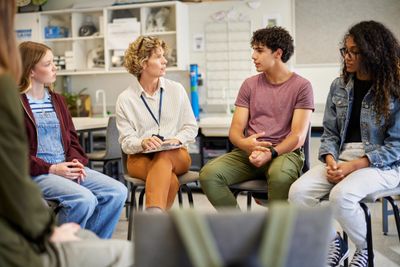 A group therapy session with a counselor and teenagers sharing in a circle.
