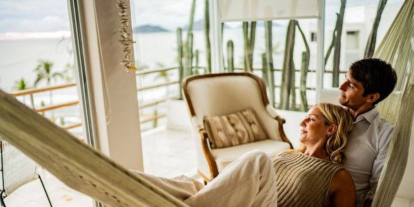 Couple relaxing together in a hammock on a balcony with a scenic view.