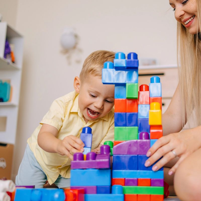 A young child and an adult enjoy stacking colorful toy blocks together in a playful home environment, fun and educational activities.